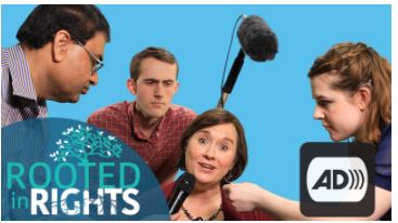 Woman looking overwhelmed, man holding microphone overhead, two others watching